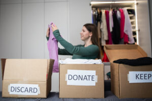 woman sorts through her wardrobe. Three craft cardboard boxes of keep, discard, donation, donate. Charity clothing donations, help low income families, recycling, declutter, sustainable